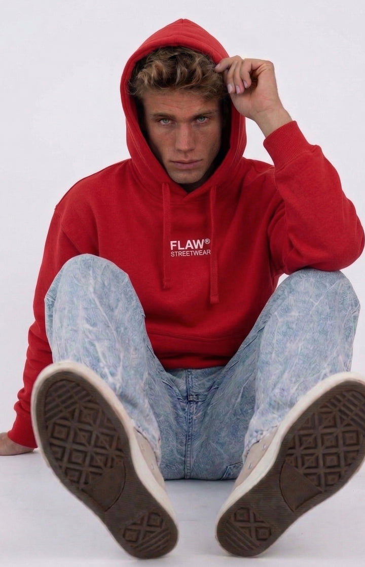 Modelo sentado usando polerón canguro oversized rojo FLAW con logo frontal