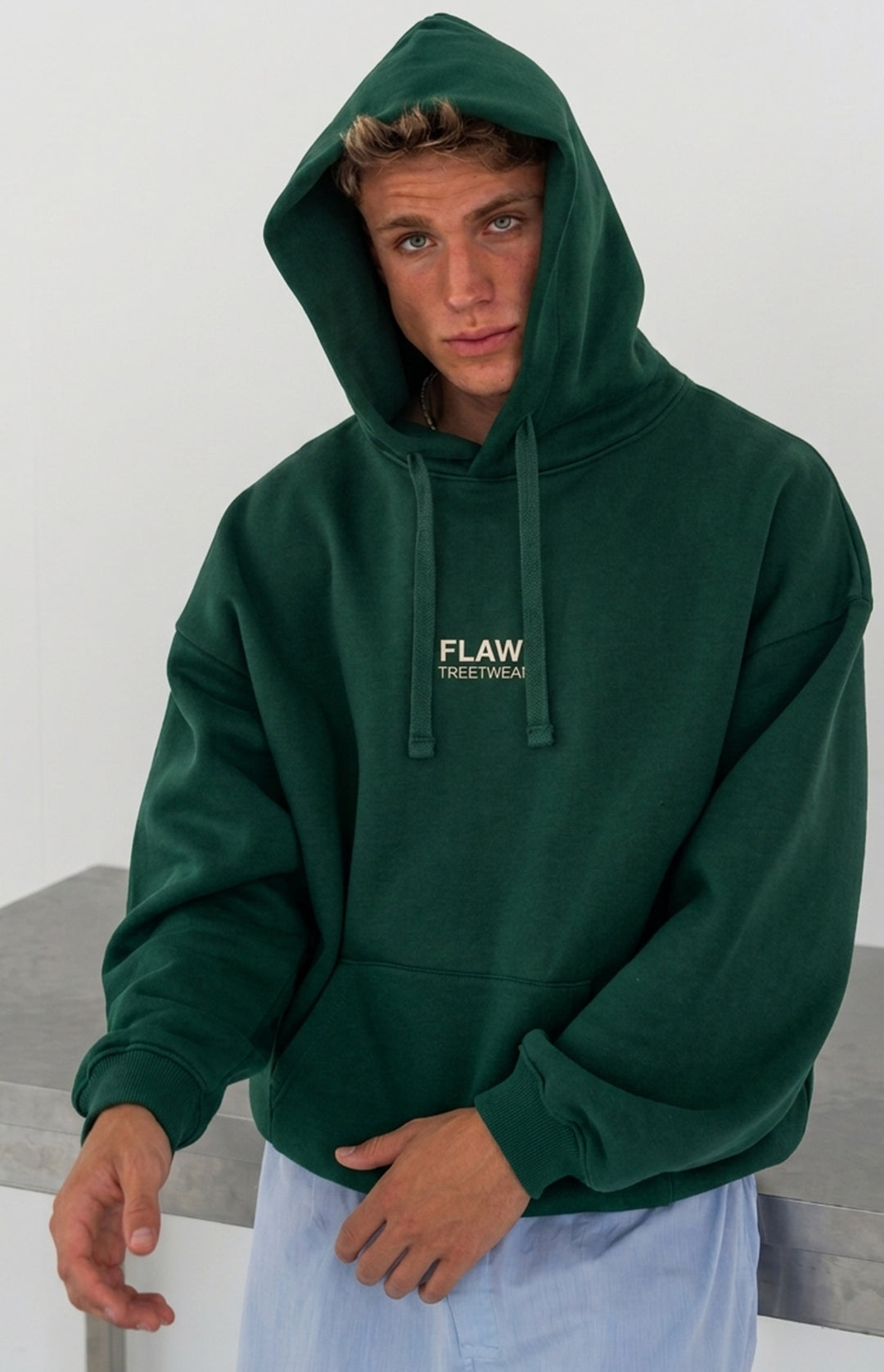 Modelo usando polerón canguro oversized verde FLAW con logo frontal Streetwear